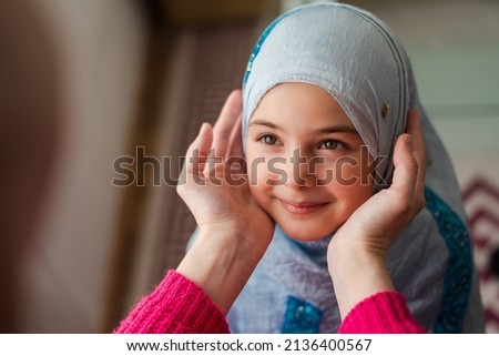 Happy Muslim family. Mother holding her child daughter in hand. Mom and daughter in hijabs smiling together in home.	Kid day care. Mother love.