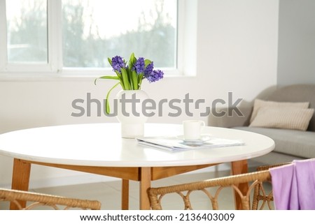 Newspaper, cup with coffee and vase with flowers on dining table in light room