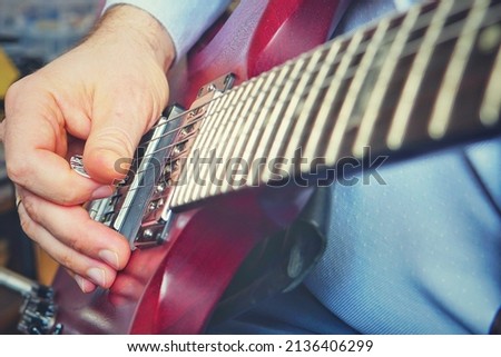 male hairy hand with wedding ring playing matte red electric guitar