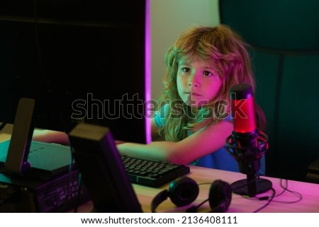 Little kid using desktop pc by night, child boy illuminated by the blue light of a computer screen. Gamer play desktop computer game. Gaming stream and blogging for kids. Social media for kids.