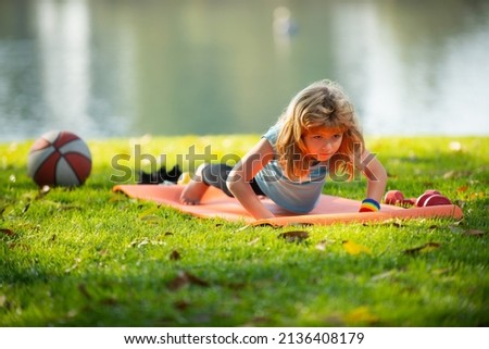 Child doing gymnastic exercises, sportive kid doing push ups on fitness mat in nature. Boy doing push-ups in the yard. Kid pushing up. Royalty-Free Stock Photo #2136408179