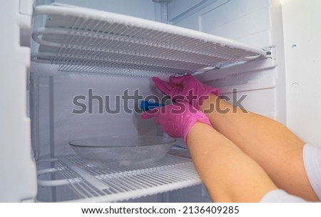 Defrosting and cleaning the freezer. A woman in latex gloves wipes meltwater with a sponge. Shallow depth of field.  Royalty-Free Stock Photo #2136409285