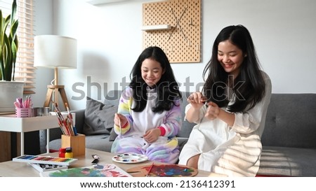 Smiling teenage woman and her young sister enjoy painting picture while spending leisure time together at home.