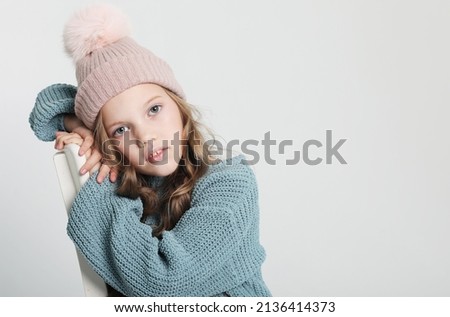 Happy little girl wearing blue sweater and winter hat on white background
