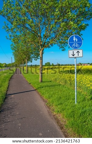 Beautiful farm landscape with rapeseed blossom field and a cycling and hiking lane or path in Germany, Spring, at sunny day and blue sky, with a signpost for bicycles and people