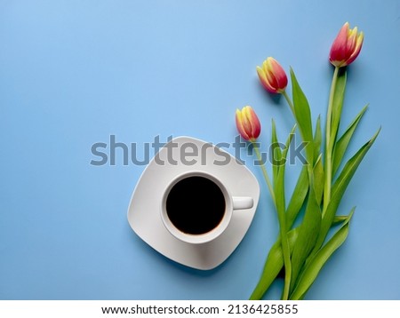 Morning with cup of hot coffee and yellow, red tulips on blue background. Top view, copy space, mockup. Flat lay. Food and drinks. Spring holidays. 