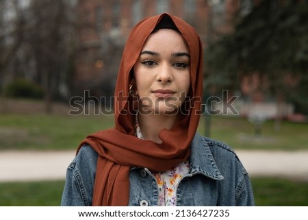 Cinematic shot of young happy Arabian muslim woman wearing hijab is looking  in camera outdoors. Royalty-Free Stock Photo #2136427235