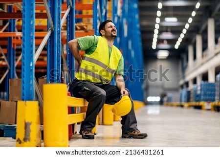 A storage worker in pain having back pain and massage the painful place. Royalty-Free Stock Photo #2136431261