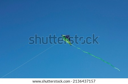 Green kite toy on a warm sunny summer day with clear blue sky without clouds fly in the wind in the middle of the picture