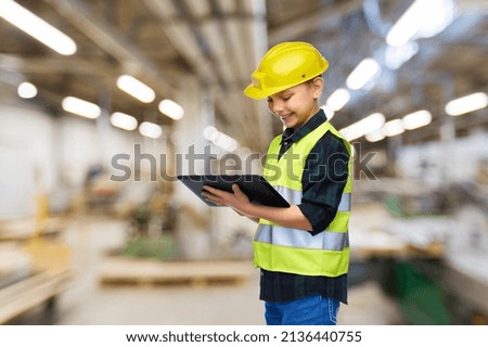 industry, manufacture and profession concept - happy smiling little boy in protective helmet and safety vest with tablet pc computer over workshop background