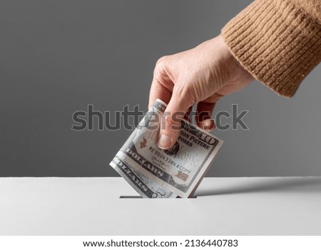 charity, financial support and saving concept - close up of hand putting money into donation box Royalty-Free Stock Photo #2136440783