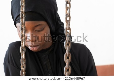 Scared young African girl behind chains, symbol of domestic abuse, child or forced marriage, gender disequality Royalty-Free Stock Photo #2136448967