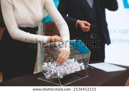 Process of prize drawings, extracting a winning numbers of lottery machine, raffle drum with bingo balls and winning tickets on event with a host and hands on lottery machine Royalty-Free Stock Photo #2136452151