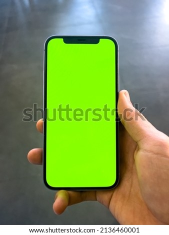 Man's hand shows mobile smartphone with green screen in vertical position
