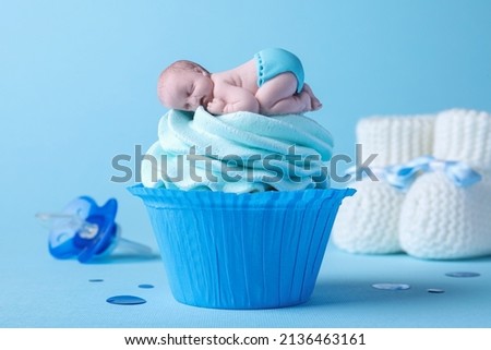 Beautifully decorated baby shower cupcake with cream and boy topper on light blue background, closeup