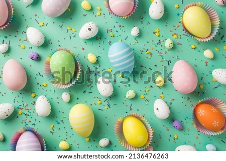 Top view photo of easter decorations multicolored easter eggs in paper baking molds and confectionery topping on isolated turquoise background