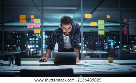 Successful Handsome Creative Director Working on Laptop Computer in Big City Office Late in the Evening. Businessman Preparing for a Marketing Plan in Conference Room. Royalty-Free Stock Photo #2136489025