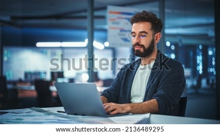 Modern Office Businessman or Manager Working on Computer, Smiling, Looking at Camera. Portrait of Successful IT Software Engineer in Glasses Working on a Laptop at his Desk. Royalty-Free Stock Photo #2136489295
