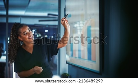 Company Operations Director Holds Sales Meeting Presentation for Employees and Executives. Creative Black Female Uses TV Screen with Growth Analysis, Charts, Ad Revenue. Work in Business Office. Royalty-Free Stock Photo #2136489299