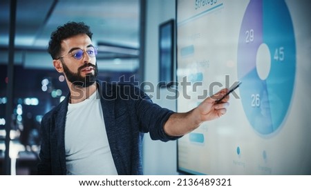 Company Creative Manager Holds Sales Meeting Presentation for Employees and Executives. Hispanic Male Uses TV Screen with Growth Analysis, Charts, Ad Revenue. Work in Business Office.