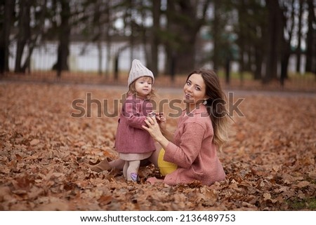 Little beautiful girl with her beautiful mother outdoors in blossom. Family daughter and mother kissing and embracing in street. Happy smart family in park