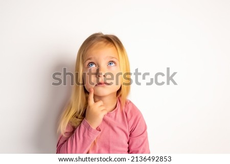 Little cute girl looks up with interest. The concept of children's curiosity and naivety. Huge blue eyes turned towards the unknown. The girl thought seriously. Royalty-Free Stock Photo #2136492853
