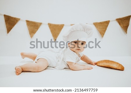 A young child in a chef's apron and hat plays the role of a baker. The table is full of clutter. The mood is sublime. There are many ingredients and different things around. Concept for bakery.