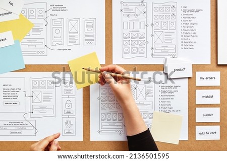 Web UX designer working on mobile responsive website project. Flat lay image of numerous website wireframe sketches and card sorting technique over product designer desk.  Royalty-Free Stock Photo #2136501595