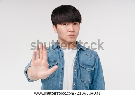 Serious young asian korean man boy student showing stop gesture with a palm isolated in white background. Forbidden, prohibited concept. Royalty-Free Stock Photo #2136504031
