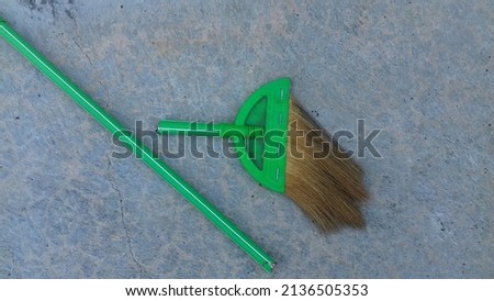 green plastic broom whose handle is broken in half is placed on a cement tile