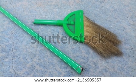 green plastic broom whose handle is broken in half is placed on a cement tile