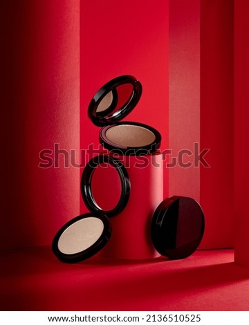 Face highlighter compact makeup powder  cases with mirror. Cosmetic products advertisement on red decorative background with decorated tubes Royalty-Free Stock Photo #2136510525