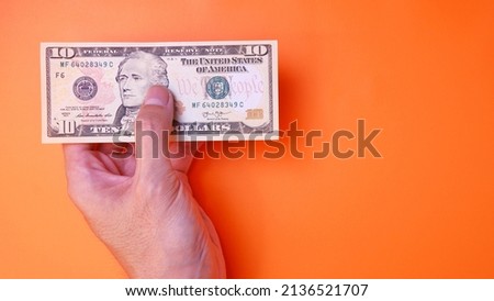 Man's hand is making a payment. Business Investment Economy Saving Loan Income Money and Finance concept. Male hand showing dollar cash on a orange background. 10 Dollar Ten USD. Prosperity concept.