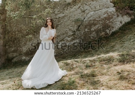 beautiful bride stands on rocks in a glamorous white wedding dress