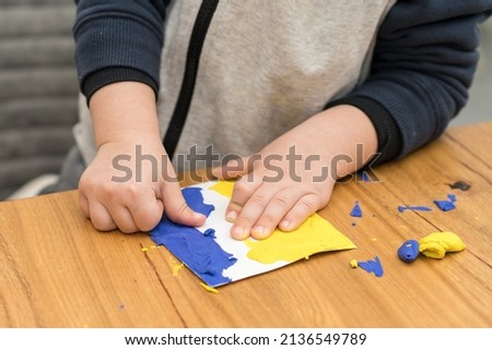Support for Ukraine. Close up little child hands makes Ukraine flag out of plasticine. Concept of patriotism, volunteering refugees, respect, charity, help, and solidarity with Ukraine.
