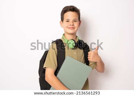 Boy wearing headphones and backpack holding a book over isolated background happy doing okay sign, thumb up with finger, excellent sign.