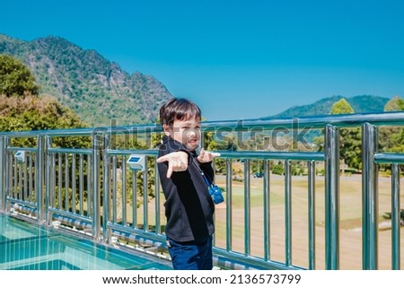 Happy little boy standing at transparent glass floor. Nature background. Soft focus. Copy space.