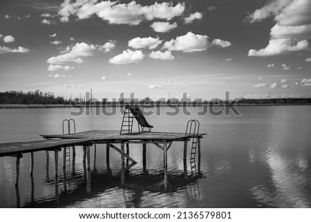 Blue water slide on the wooden dock of the lake and beautiful sky with clouds. Black and white photograph.