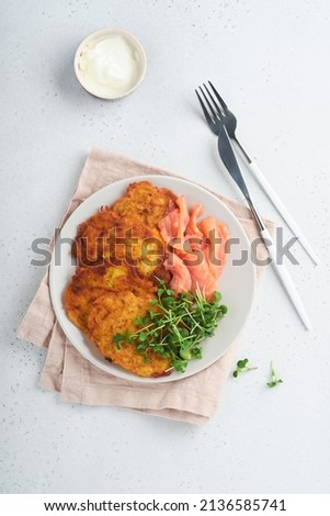 Potato pancakes. Fried homemade potato pancakes or latkes with cream, green onions, microgreens, red salmon and sauce in rustic plate on white table background. Rustic style. Healthy food. Top view.