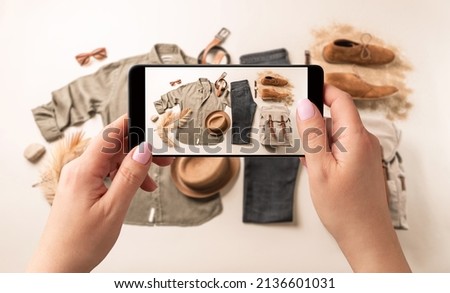 Woman taking photo of man’s casual clothes (jeans, khaki shirt) with smartphone. Blogger, influencer or stylist capturing fashion outfit and accessories for social media. 