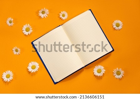 Navy blue notepad with white sheets and white daisies on summer orange background. Plans for summer to do list