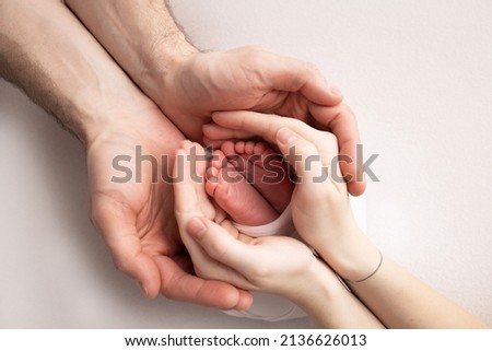 The palms of the father, the mother are holding the foot of the newborn baby. Feet of the newborn on the palms of the parents. Studio photography of a child's toes, heels and feet. Concept.