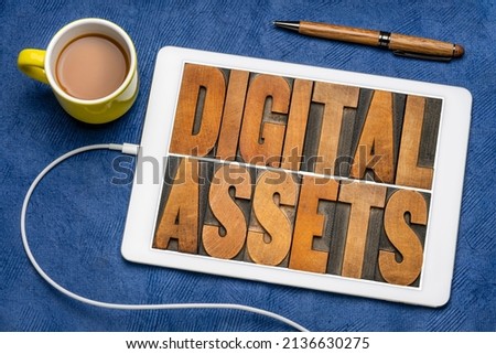 digital assets word abstract in vintage letterpress wood type on a digital tablet, flat lay with coffee, information, business and technology concept.