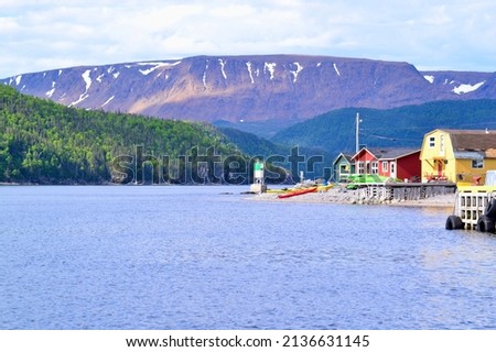 Colourful buildings along shore of Bonne Bay with the Tablelands on the horizon at Norris Point during Summer Royalty-Free Stock Photo #2136631145