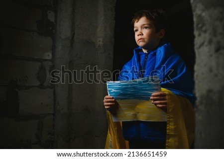 Ukrainian Crying boy holds a painted flag of Ukraine. War of Russia against Ukraine. Ukrainian Crying boy asks to stop the war in Ukraine. Child with message Stop War.