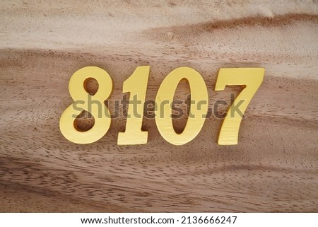 Wooden  numerals 8107 painted in gold on a dark brown and white patterned plank background.