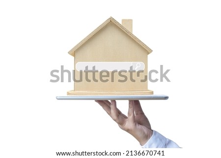 A hand holding a tablet and wooden model house with a search bar icon.