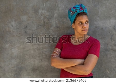 Portrait of Latin American woman (34) with scarf on her head, isolated on gray background with her arms crossed looks to her left side. Copy space. Concept promotion discount offer.