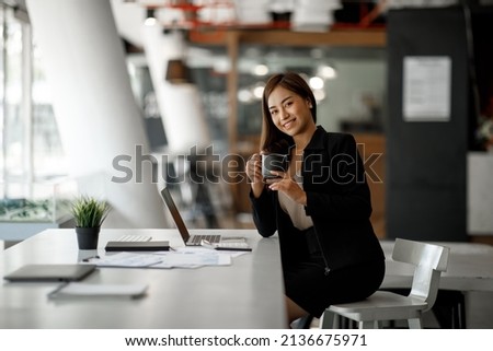 Charming Asian businesswoman sitting in the office with a digital laptop computer. Excited Asian businesswoman raising hands to congratulate while working in a modern office,
