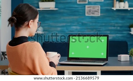 Female student looking at green screen background on laptop, working with blank chroma key template and isolated mockup copy space for online school lesson. Remote education. Tripod shot.